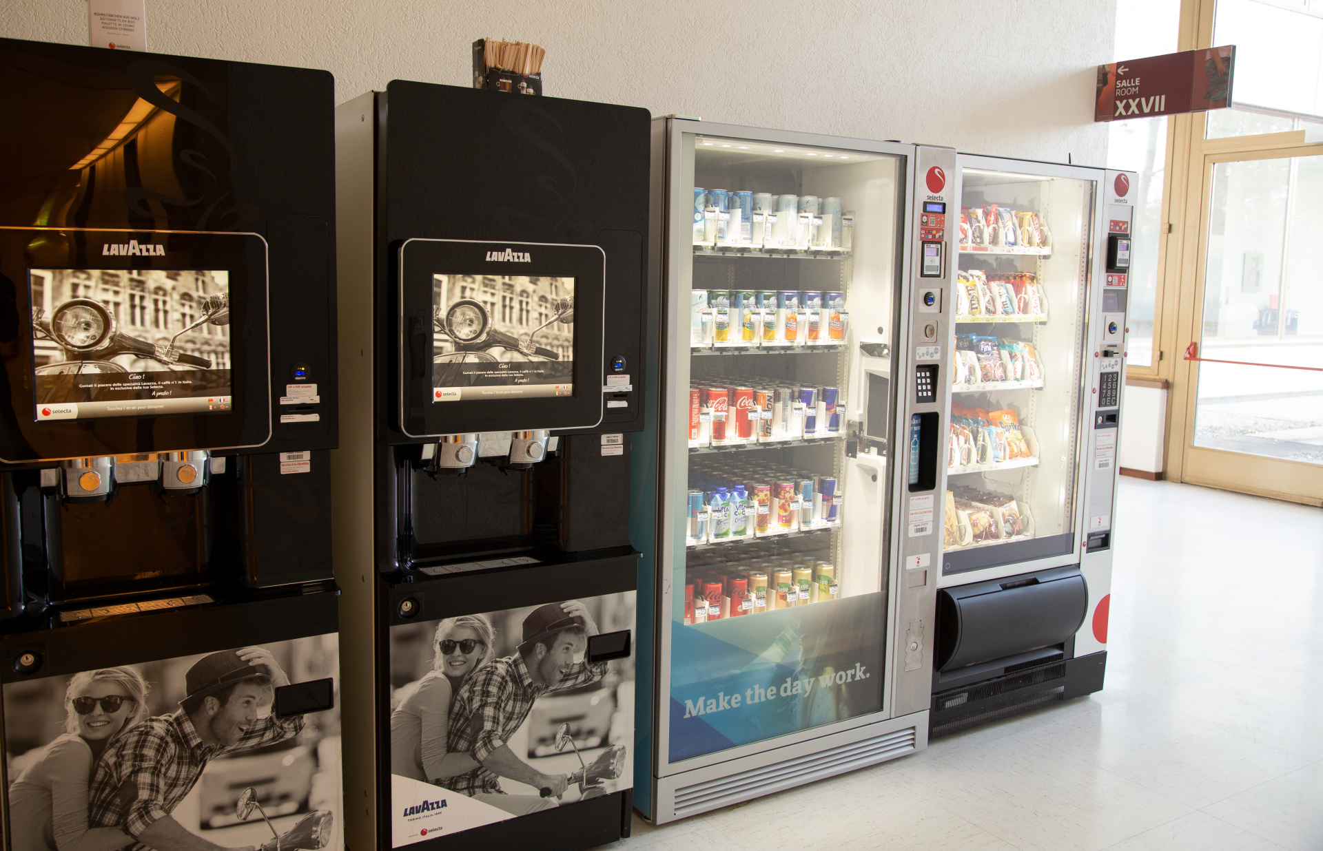 Vending machines for coffee, soft drinks, and snacks in a brightly lit hallway.