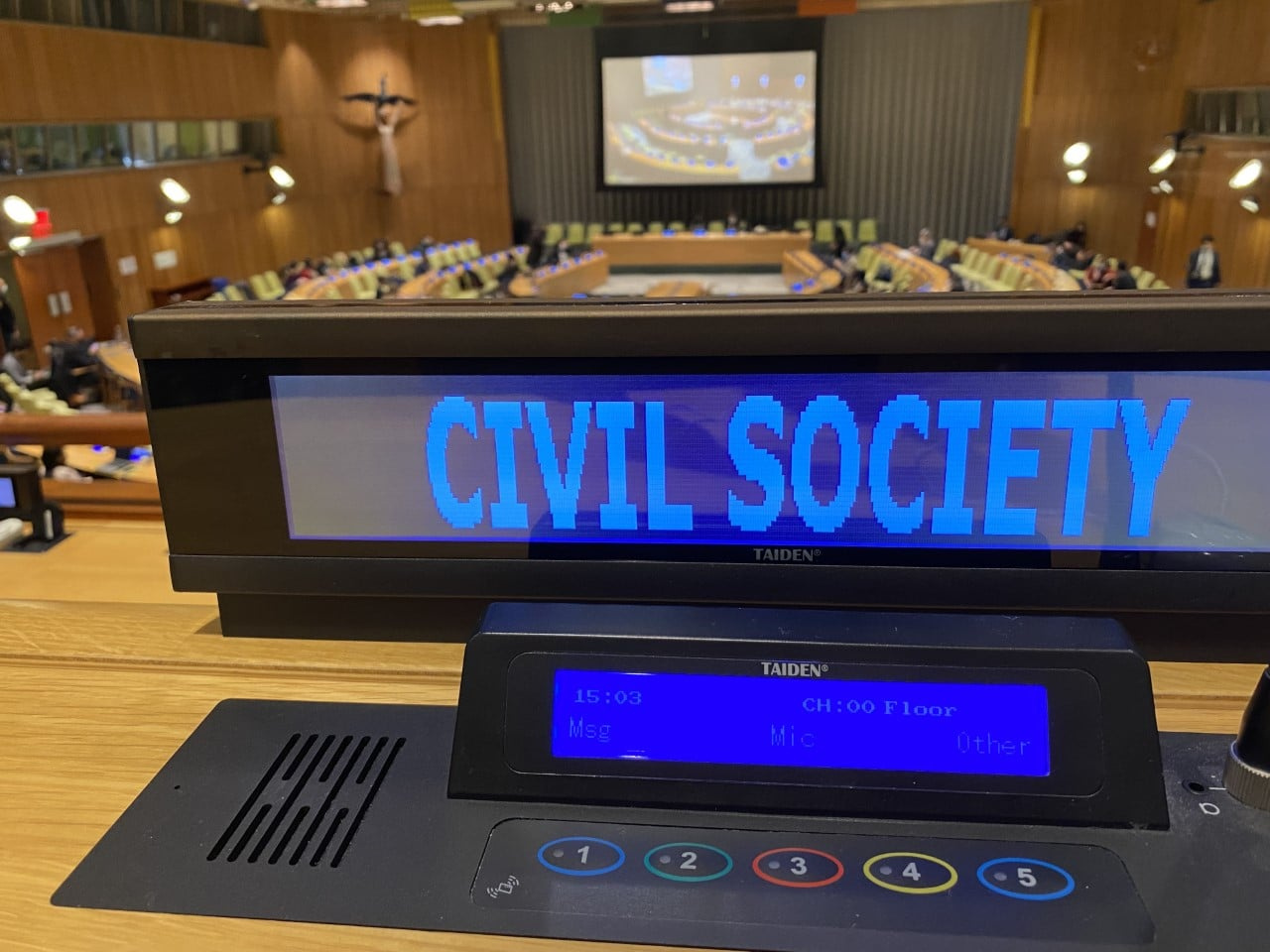 A shot of one of the meeting rooms in UNOG which is seen in the background. The foreground shows the electronic name tag on one of the seats, displaying "Civil Society"
