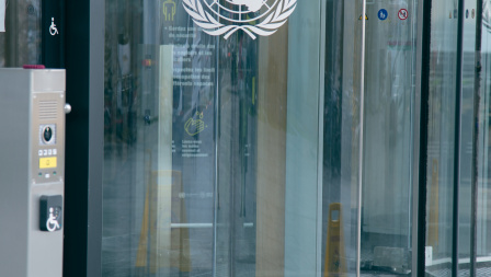 photo of the entrance to Building H at Palais des Nations, with a button to open the wheelchair-accessible door in the foreground