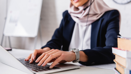 A woman typing on a laptop. She is wearing a headset. The upper part of her face is not seen as to keep her anonymous. 