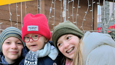 Three children are leaning towards each other, smiling into the camera.