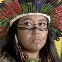 Close-up of an indigenous woman with traditional head wear and facial drawings. 