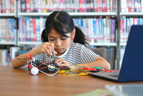 A girl sitting at a table, fully concentrated building a robot