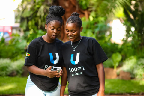 2 girls looking at a phone. They both wear a t-shirt with the words "U Report by UNICEF".