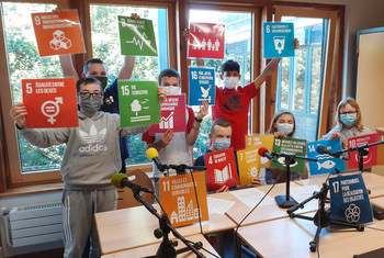 A group of masked coworkers in a brightly lit office space, showing colorful illustrations of the SDGs.