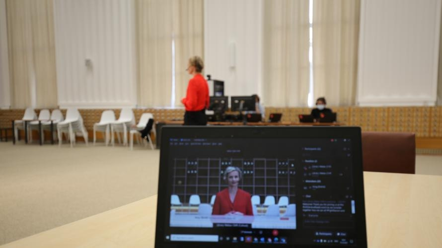 A computer shows a person speaking. In the background the person is seen blurred.