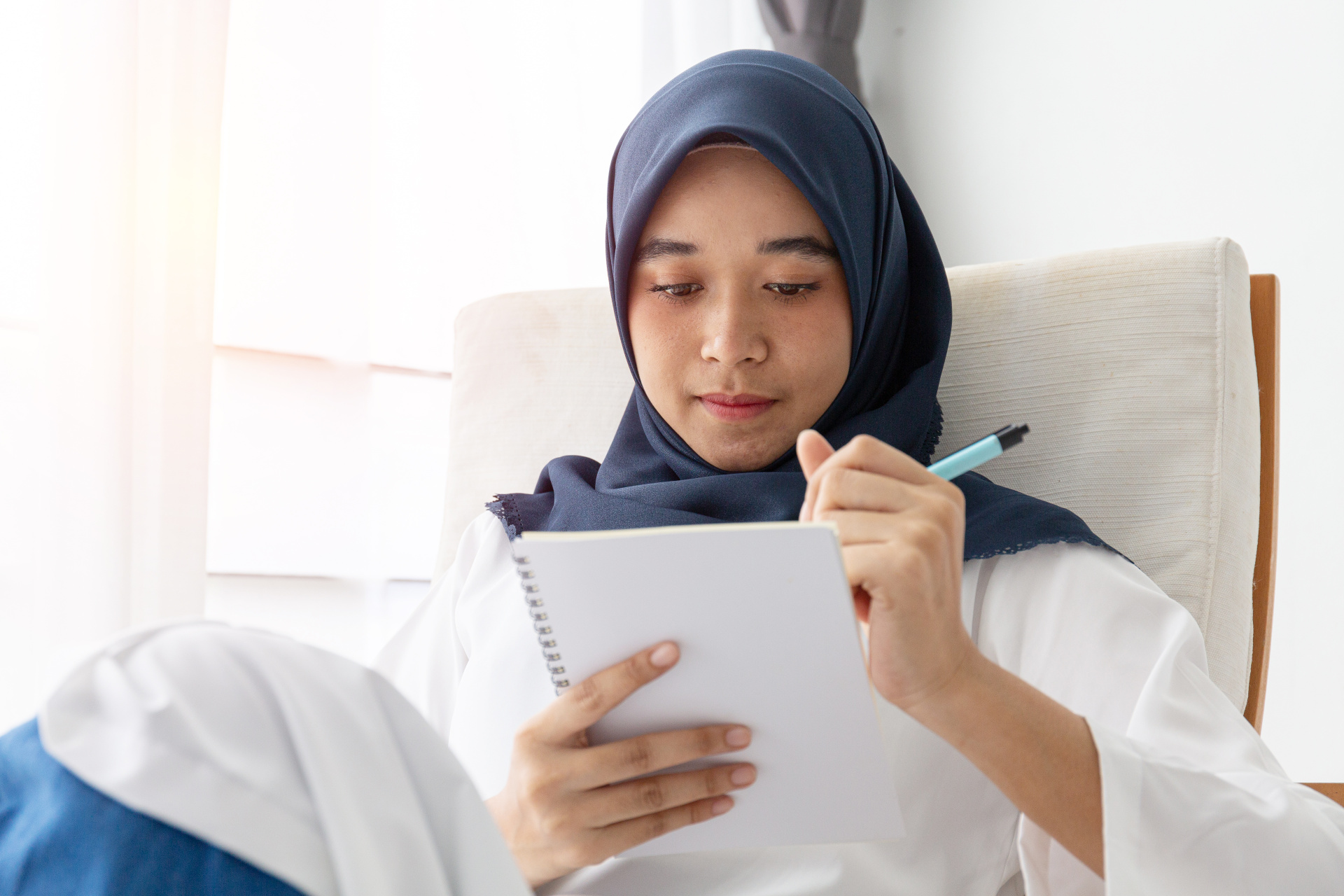 A girl sitting on a chair with a notebook, writing down her thoughts.