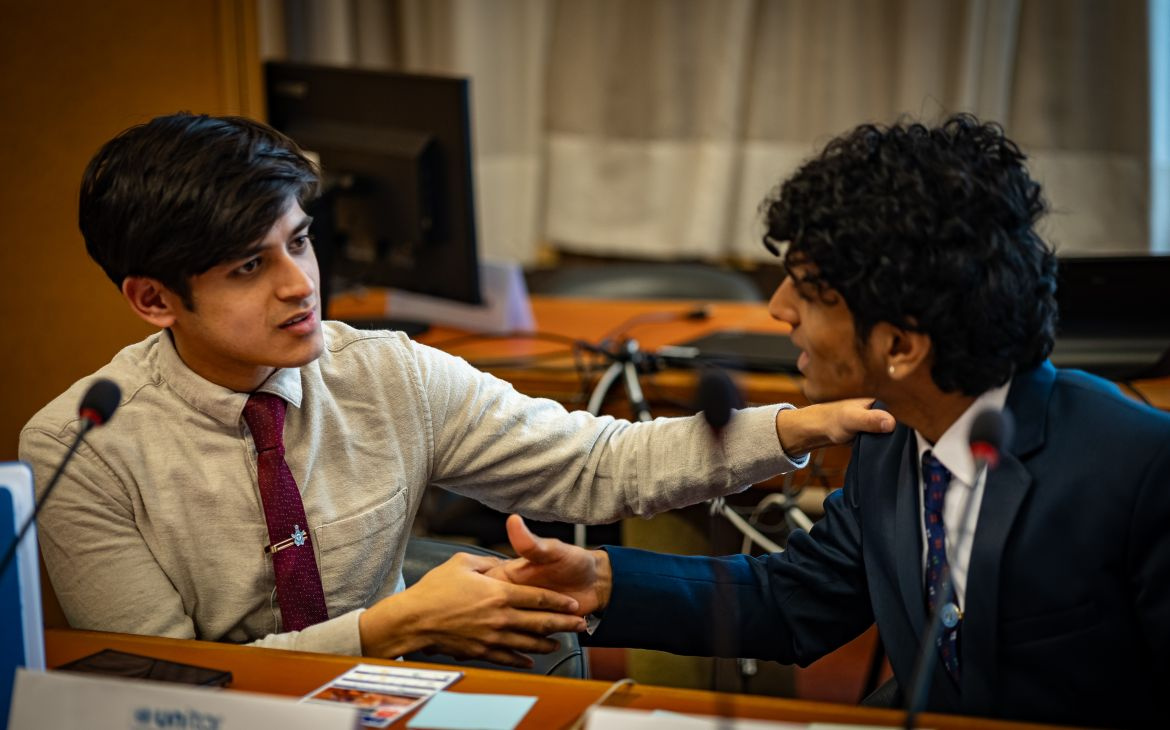 Two young men sitting in a conference room, shaking hands