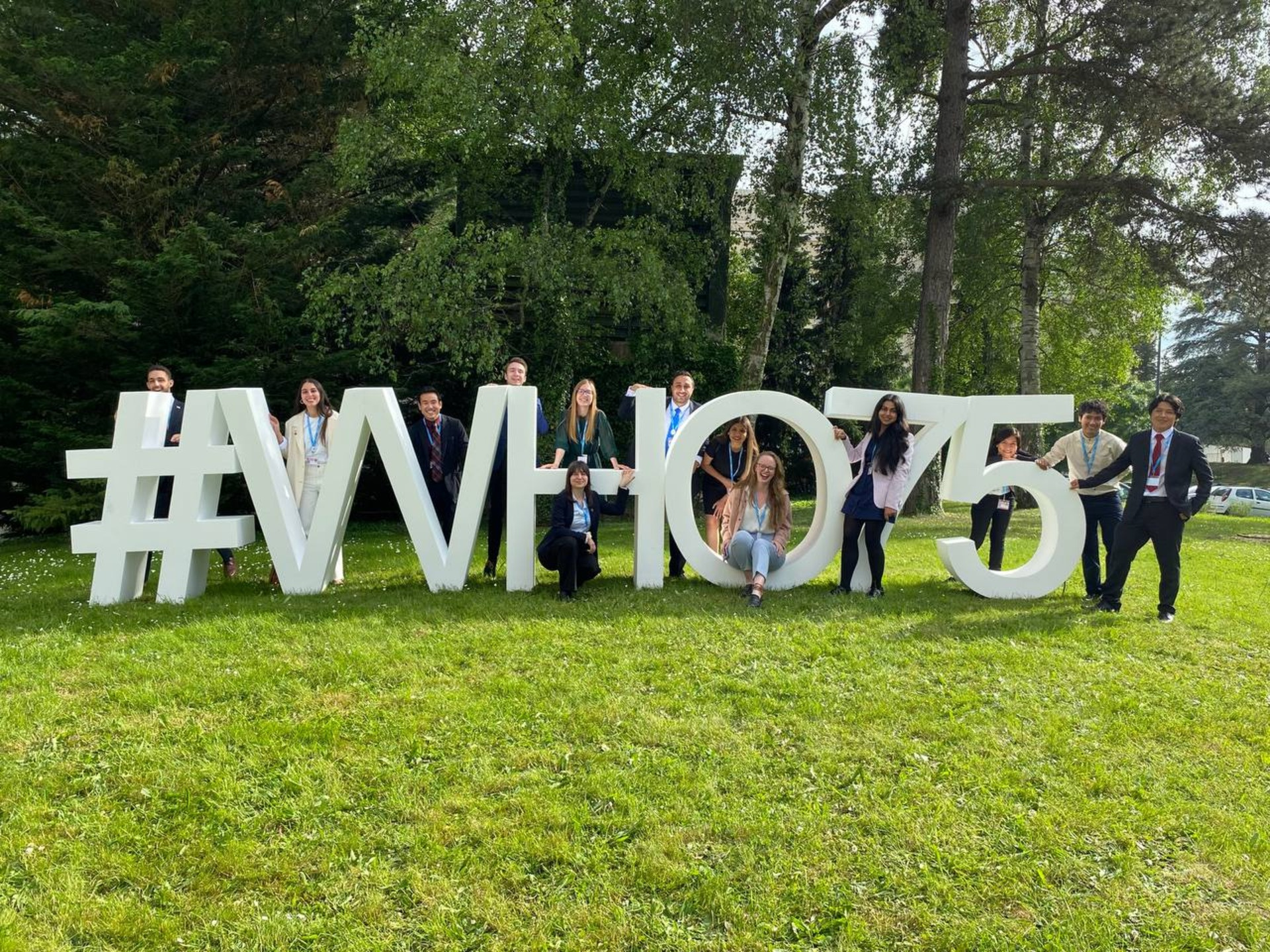 A group of young persons standing around a life size sign #WHO75.