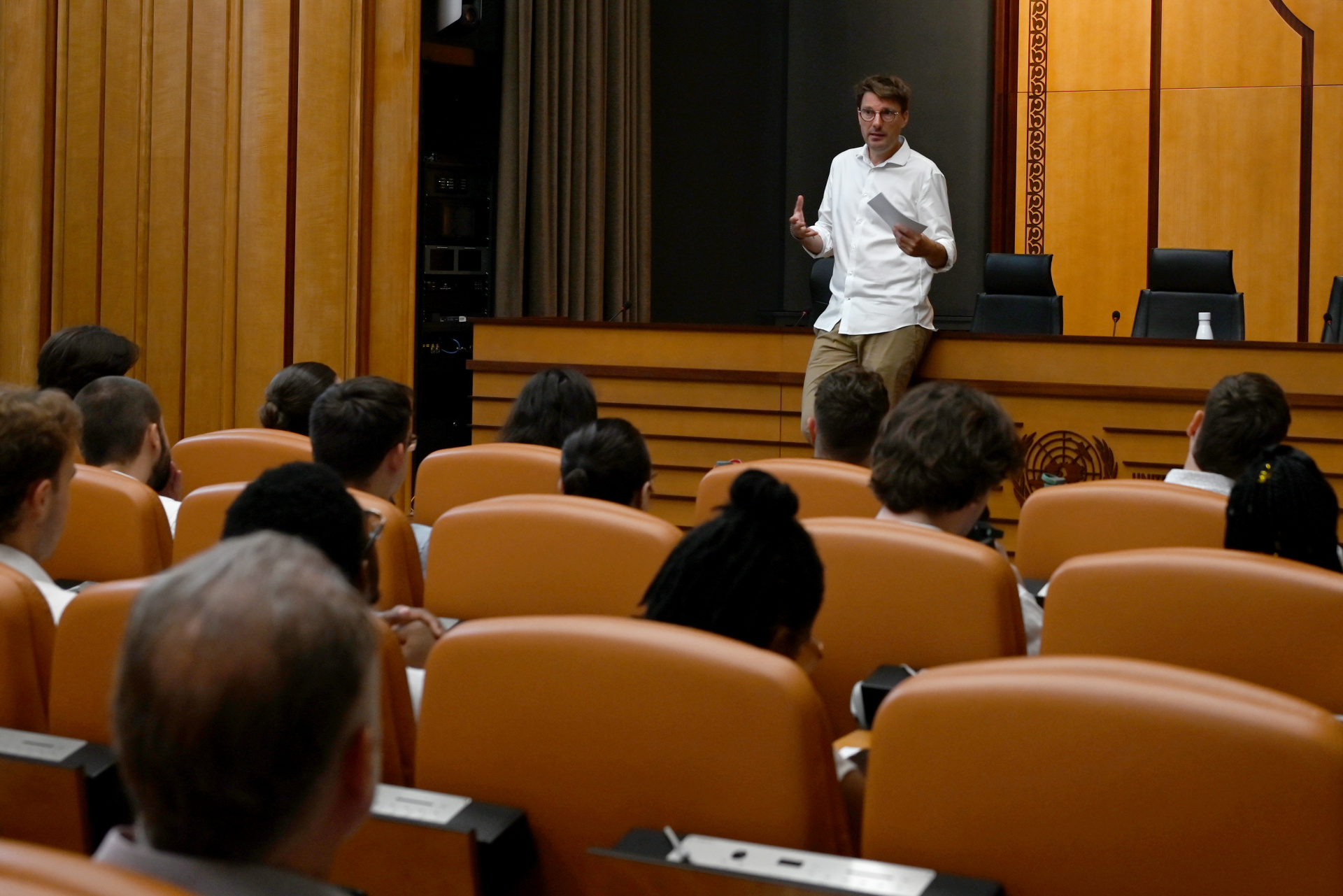 In UNOG's cinema room: a speaker addressing a group. The group is seen from behind, sitting, while the speaker stands in front of them, facing them and the camera.