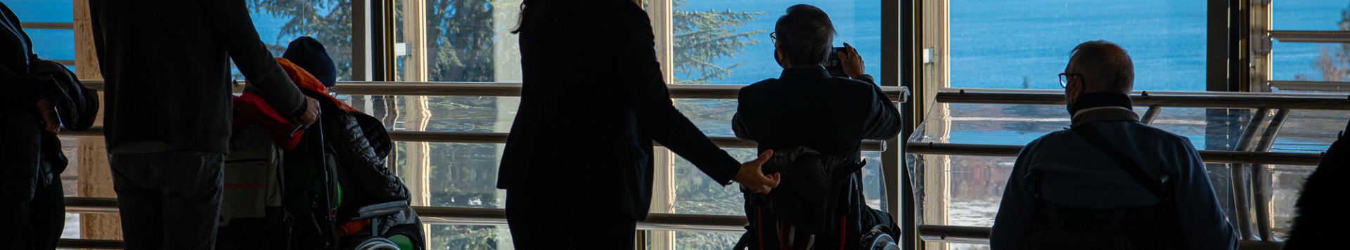 a group of visitors using wheelchairs take photos of Lake Geneva from inside the UN Geneva office.