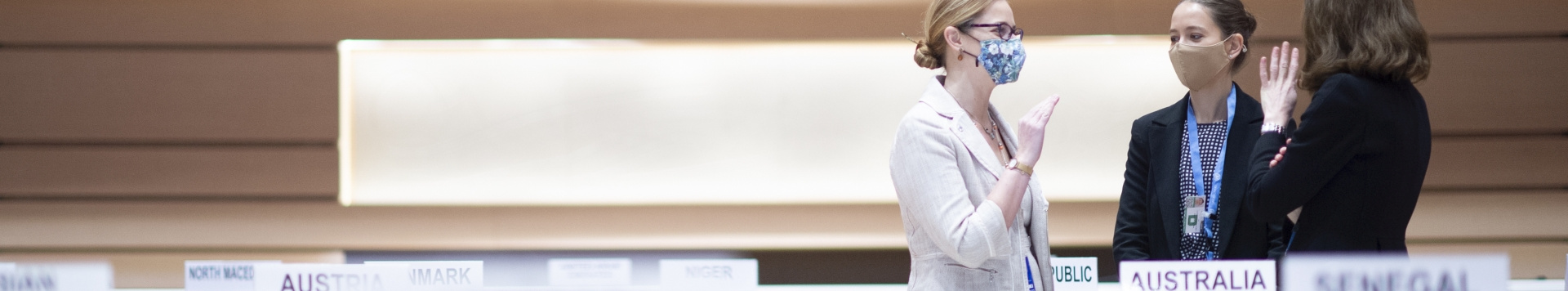 Three women are standing in one of the conference rooms of UN Geneva. They are discussing while all wearing masks.