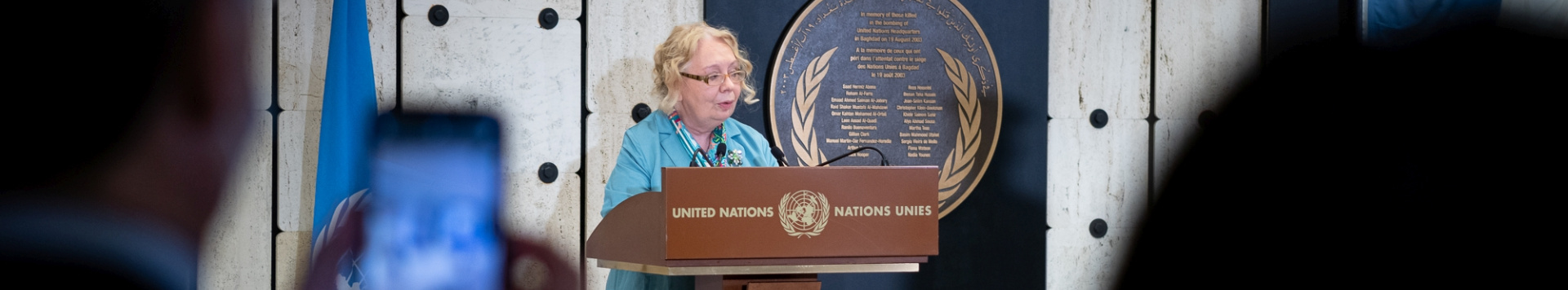 The Director-General of UN Geneva, Tatiana Valovaya, holding a speech for World Humantarian Day. She stands at a speakers desk with a UN flag and the UN logo behind.