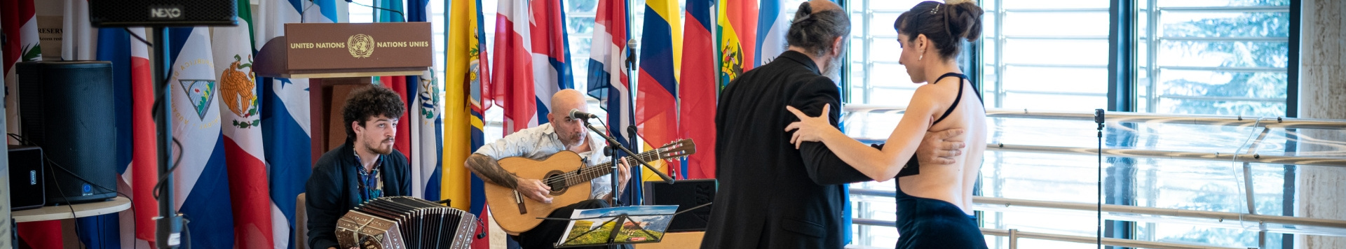 A couple is dancing in front of two musicians and several flags.