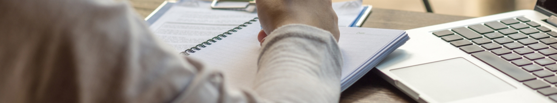 Somebody sitting with the back to the audience, only the arm is seen. The person is writing notes, a laptop standing next to the notebook.