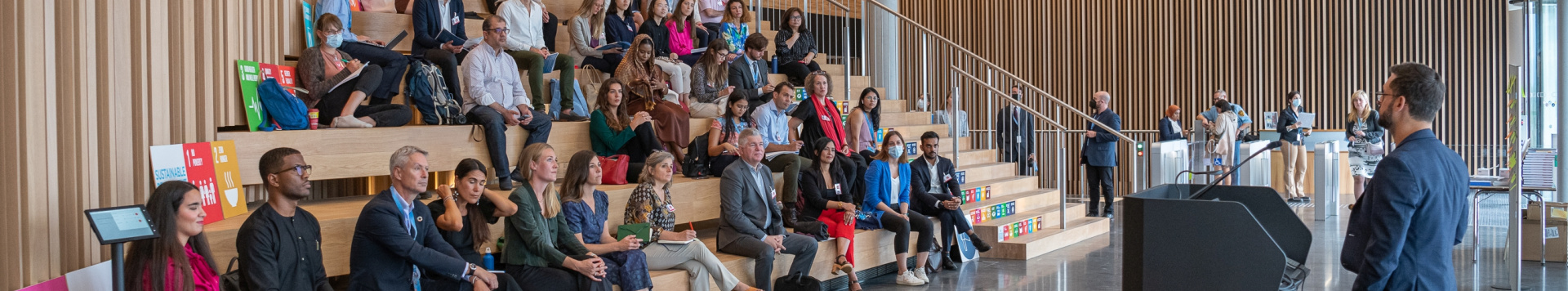 A group of persons sitting on steps to listen to a speaker.