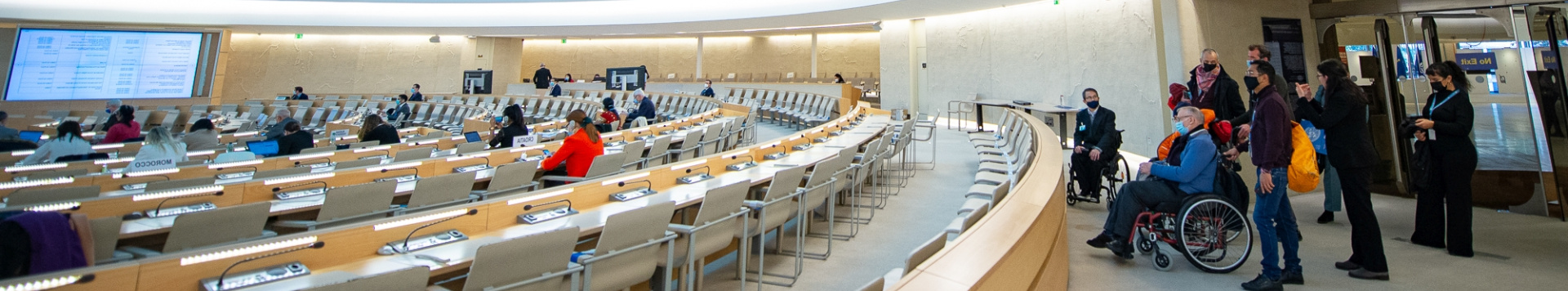 A group of people, standing and sitting in wheelchairs at the back of the Human Rights room.