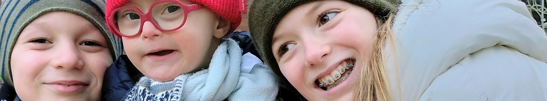 Three children are leaning towards each other, smiling into the camera.