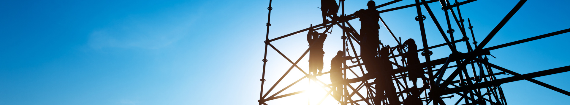 The shadow of several workers climbing on a scaffold. Only their contours are seen as the picture is taken against the sun.
