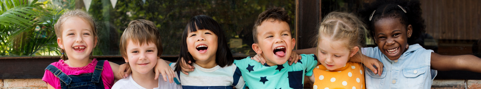 Six children sitting next to each other arm in arm, smiling into the camera