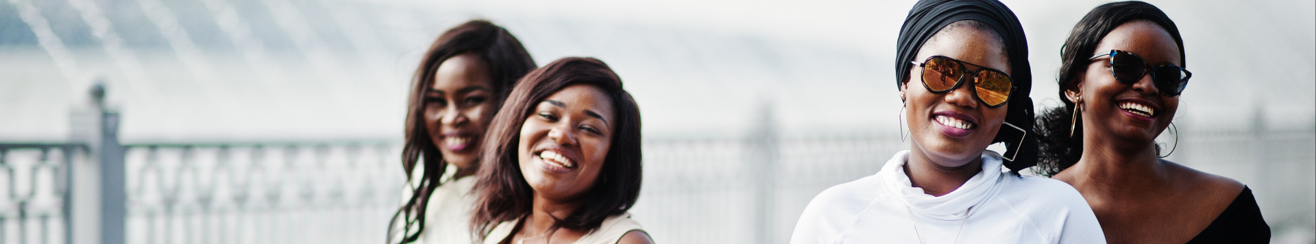 4 young women walking hand in hand towards the camera, smiling.